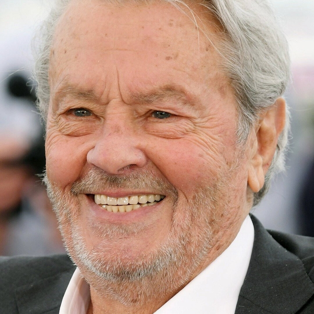 Elderly man with gray hair and a beard, smiling broadly, wearing a suit jacket and white shirt.