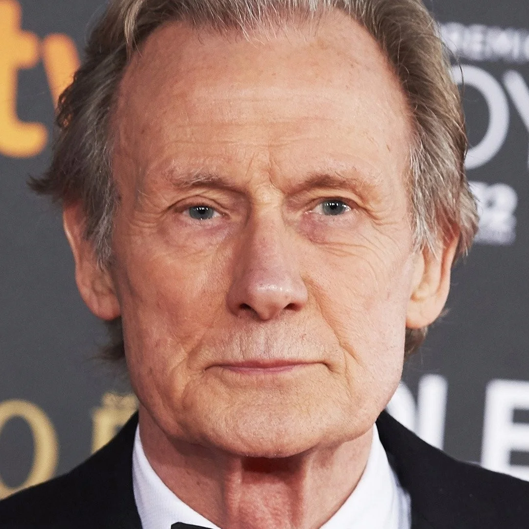 Close-up portrait of Bill Nighy with a serious expression, wearing a black suit.