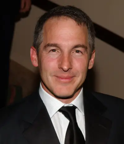 Man in a black suit and tie, smiling at the camera.