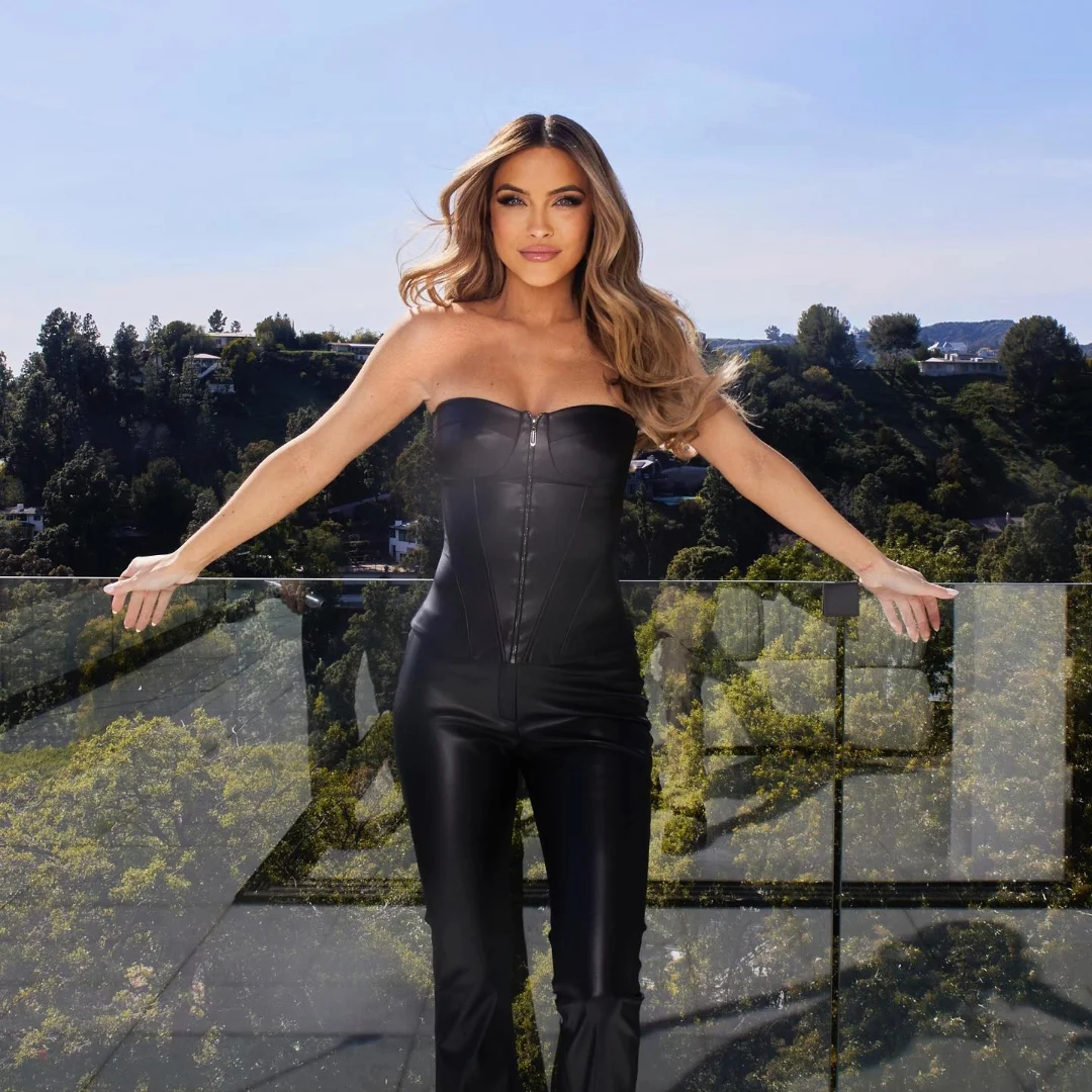 Chrishell Stause posing in a black leather outfit on a balcony with a scenic background.