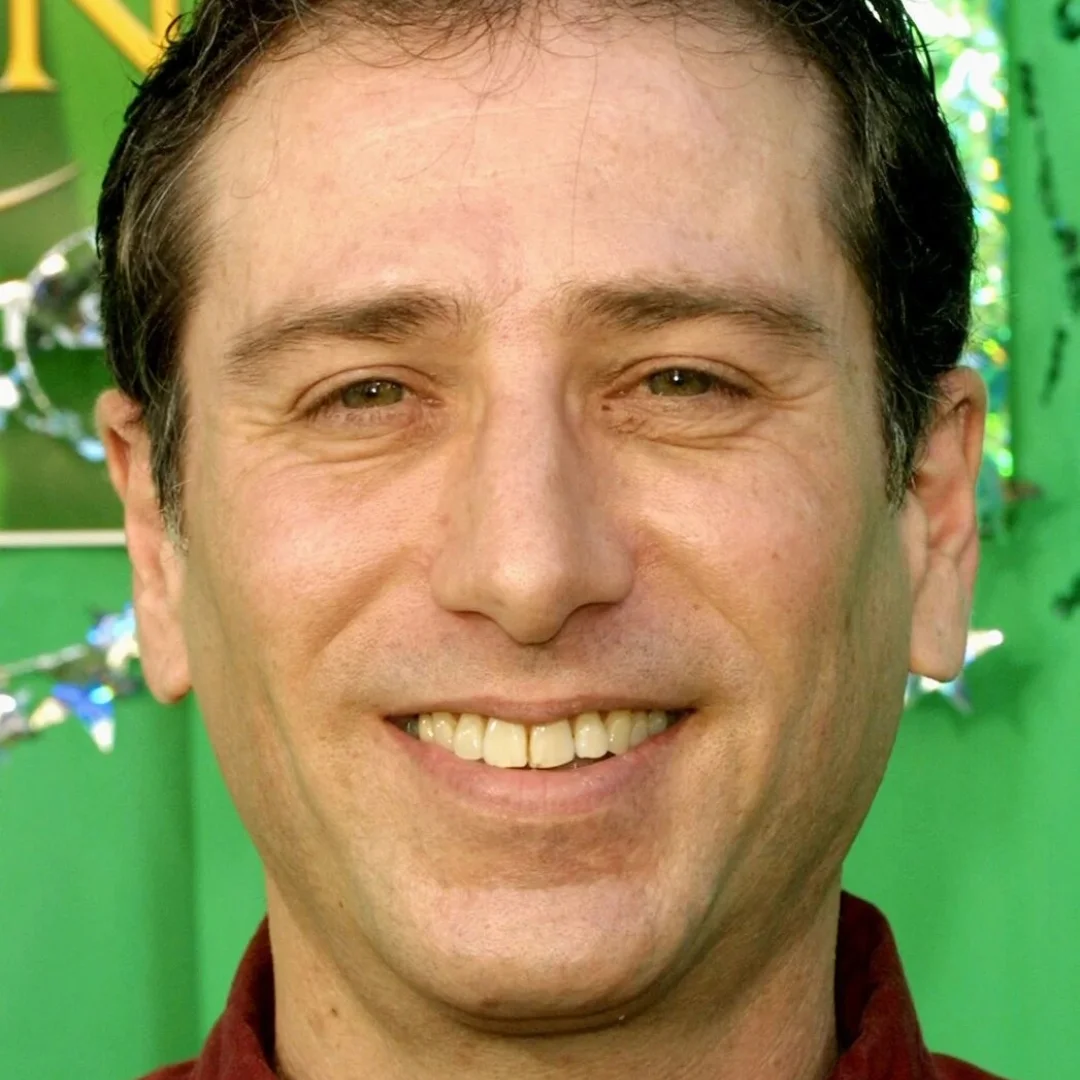 Smiling man with short dark hair and a green background