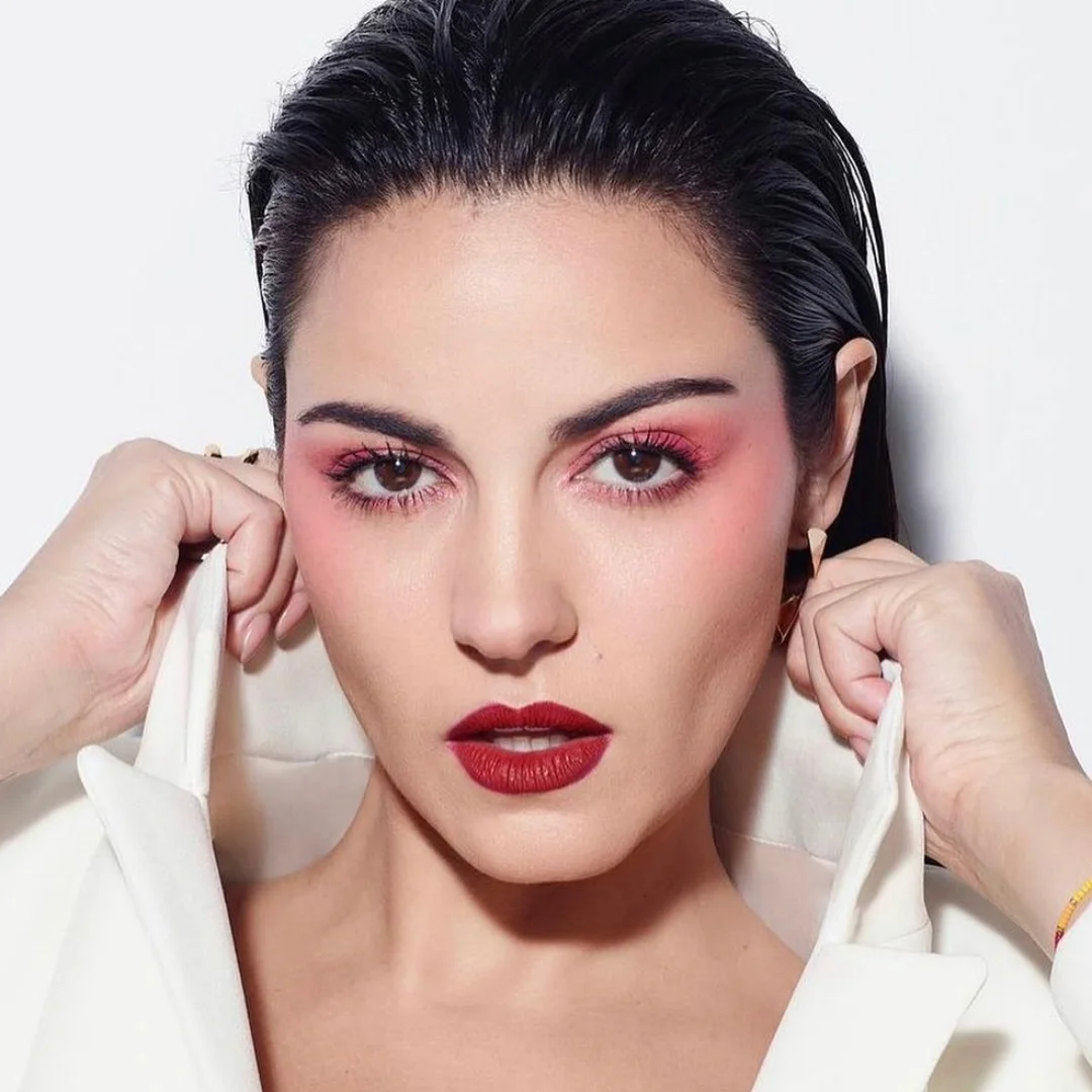 Woman with wet hair and red lipstick, pulling up the collar of a white jacket.