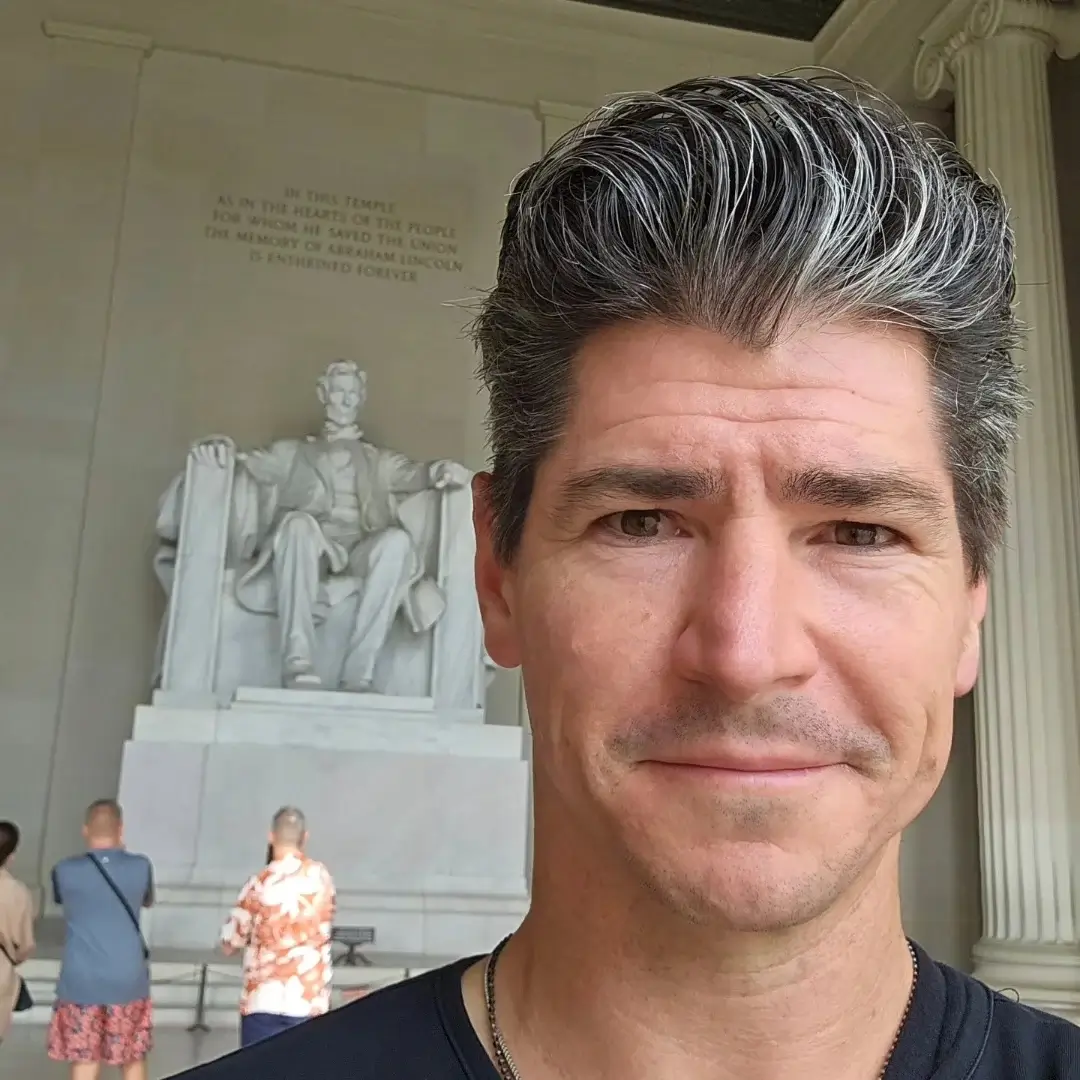 Man with gray hair standing in front of the Lincoln Memorial.