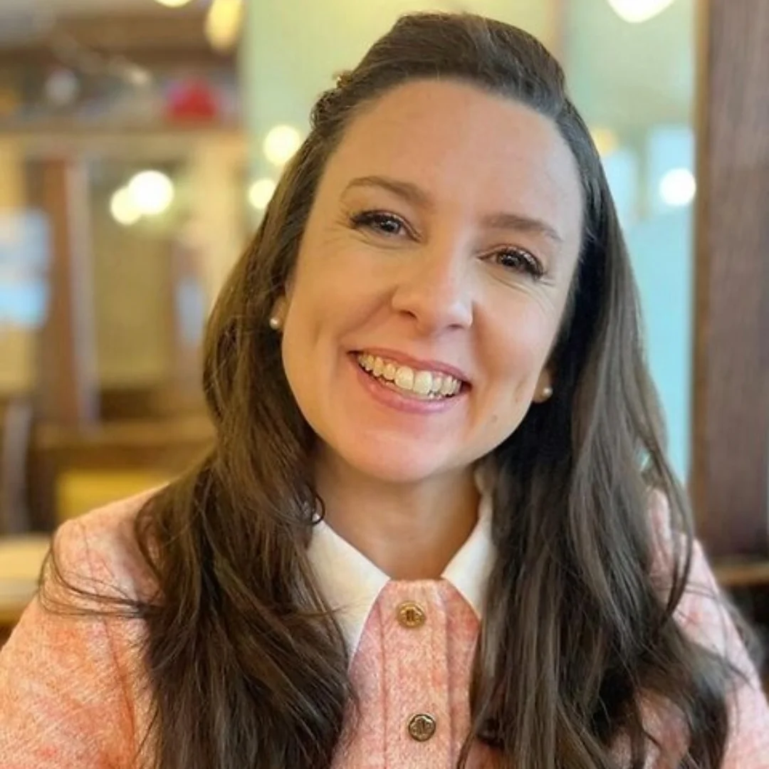 Miss Rachel, popular children's content creator, smiling in a pink outfit while sitting in a cozy cafe.