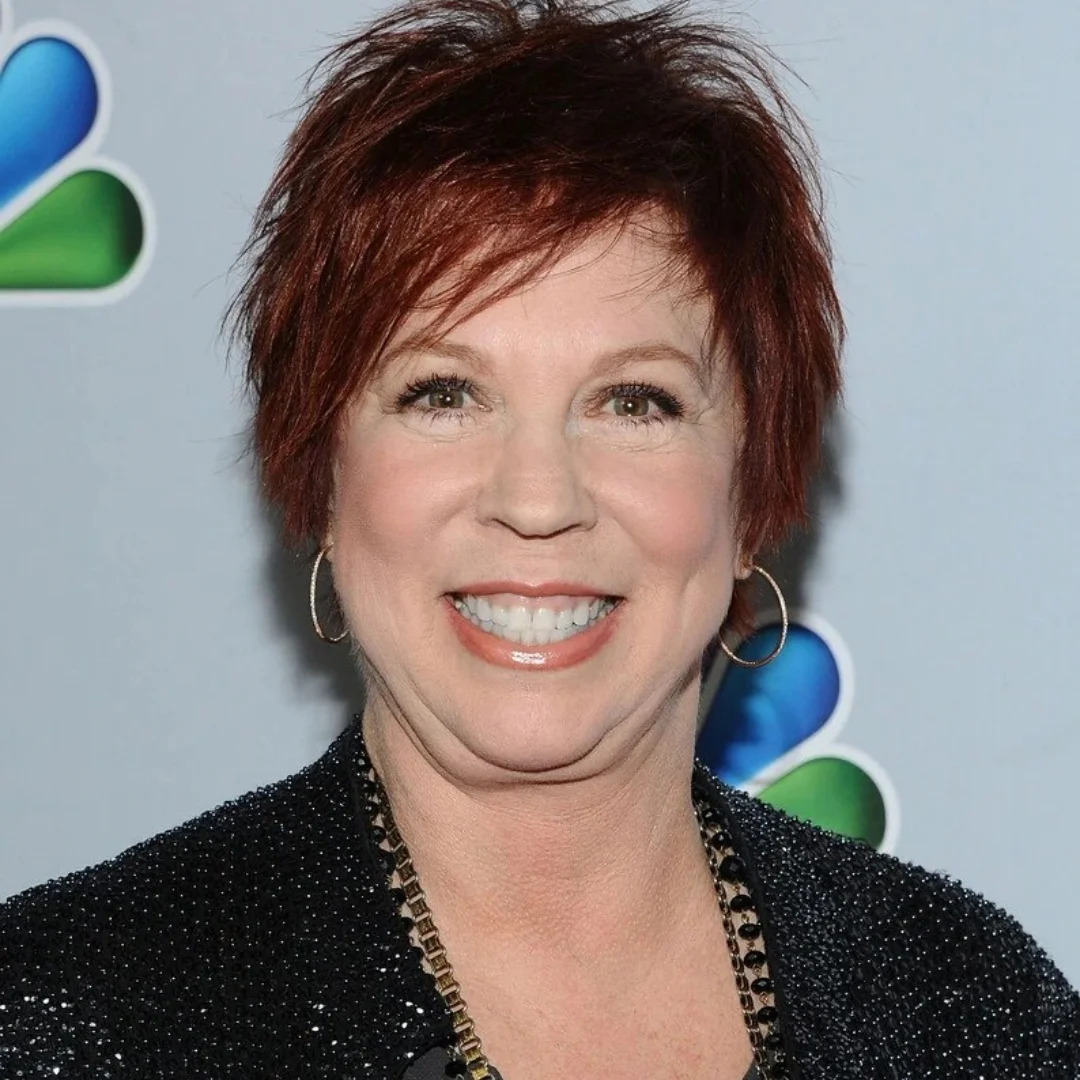 Vicki Lawrence smiling at an event with short red hair and wearing a black sequin outfit.