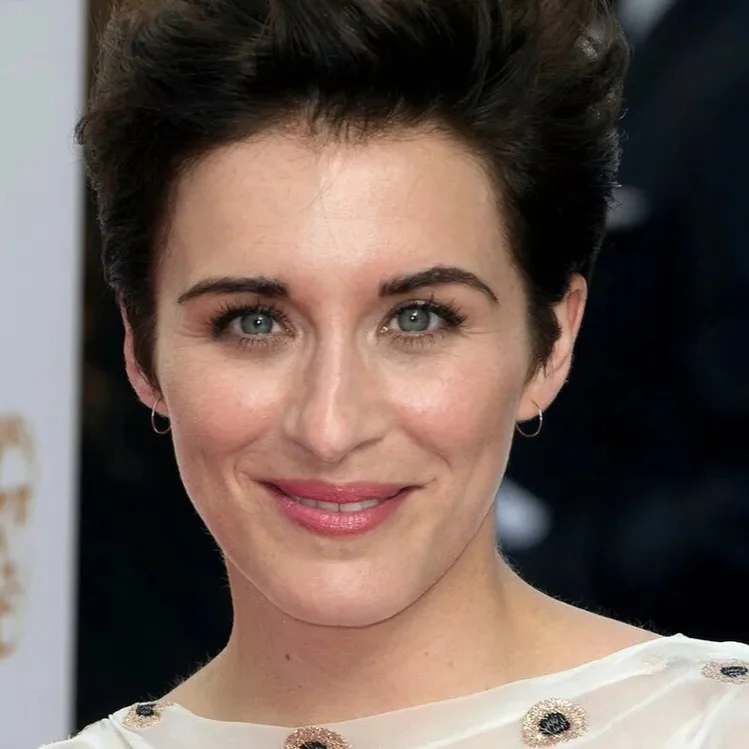 Woman with short dark hair and a white dress with floral embellishments, smiling at the camera.