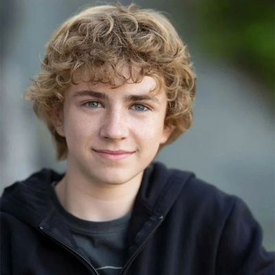 Young boy with curly blonde hair, wearing a black hoodie, smiling at the camera