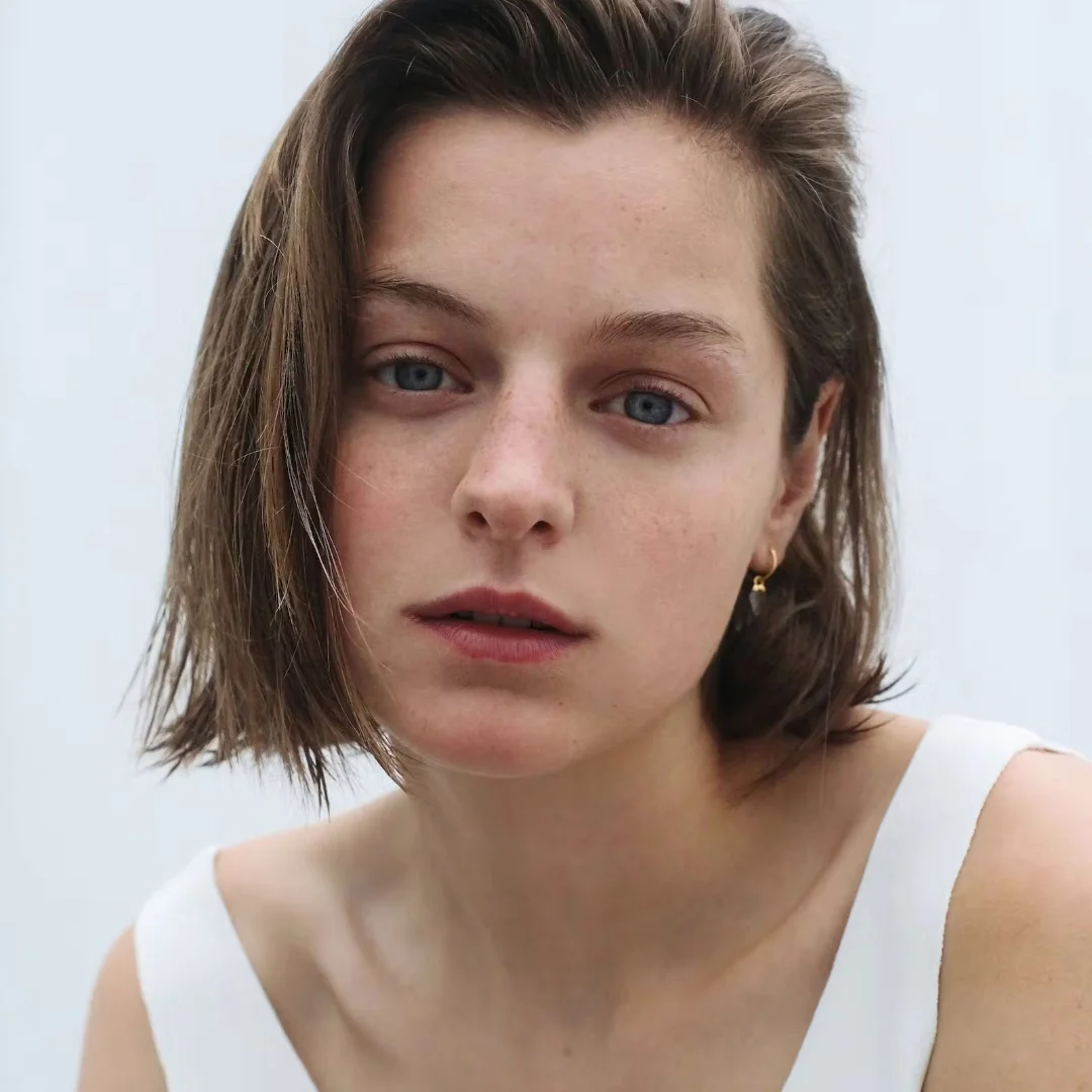 Close-up portrait of a young woman with short hair and blue eyes, wearing a white top