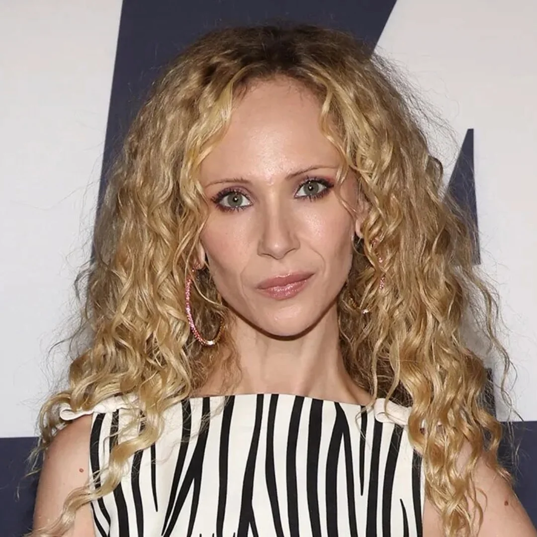 Woman with long curly blonde hair and green eyes, wearing a black and white striped outfit